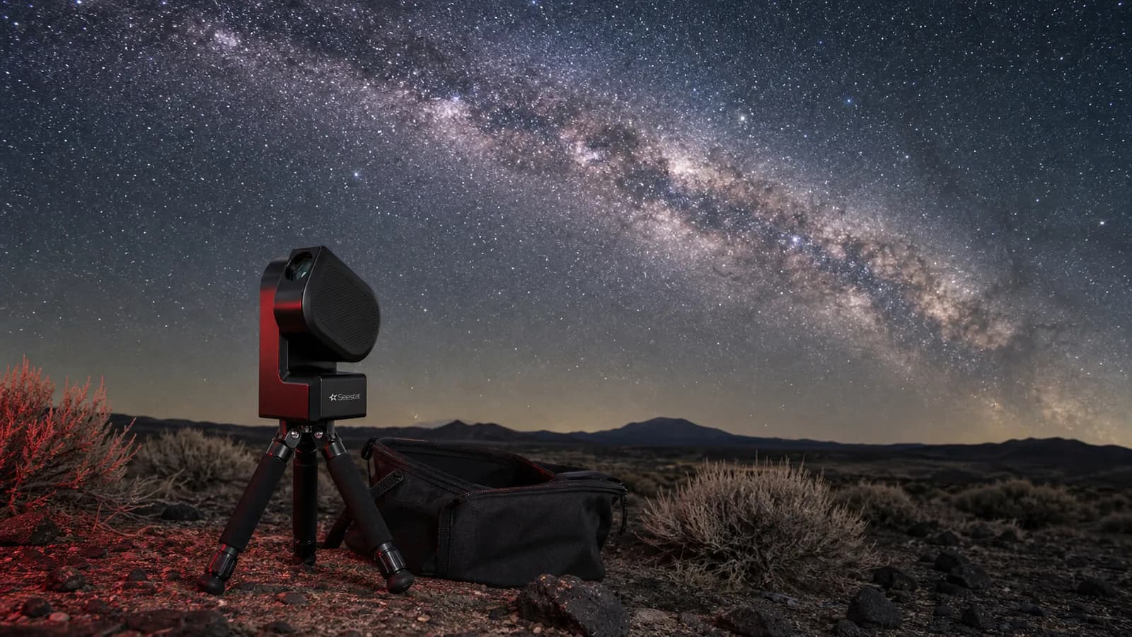 ZWO Seestar S50 set up on its tripod at a high-desert dark-sky site with the Milky Way overhead and its carry bag visible on the ground beside it